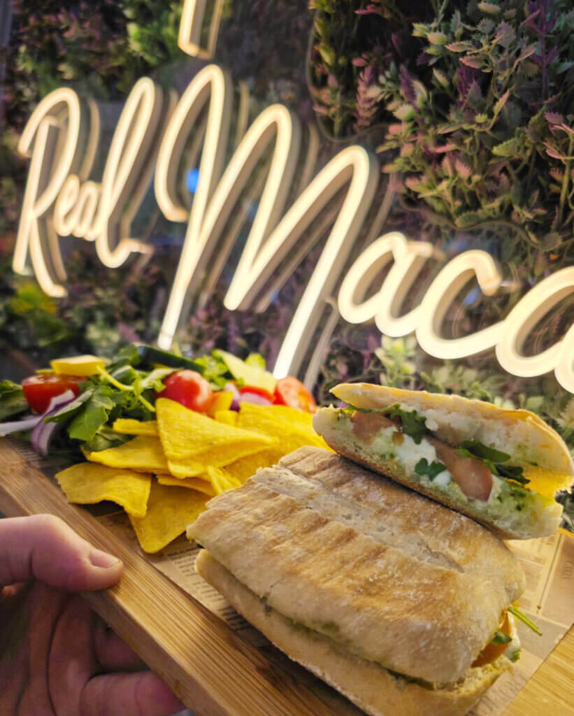 A mozzarella and pesto ciabatta sandwich served on a plate with tortilla chips and a side salad.